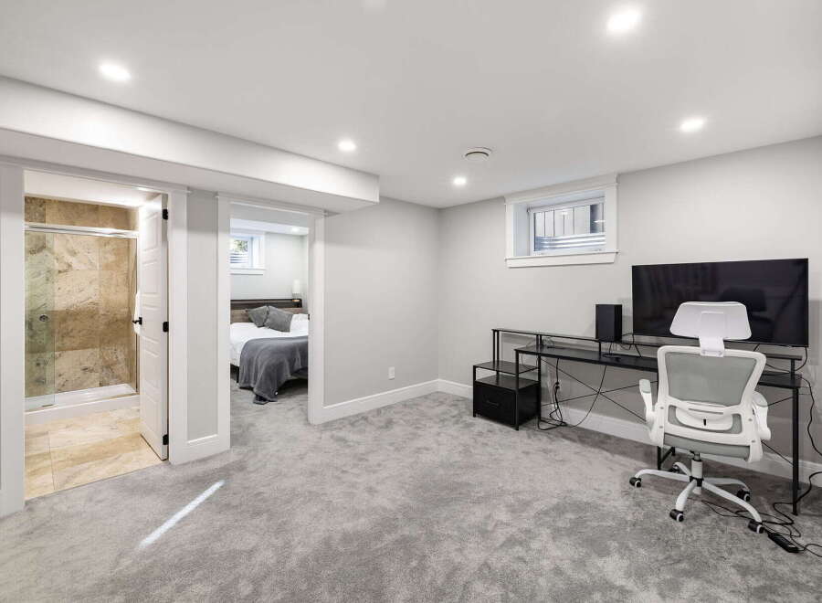 Discover comfortable living in this modern basement suite, featuring a spacious bedroom with a cozy grey duvet and a private ensuite bathroom with a walk-in shower.