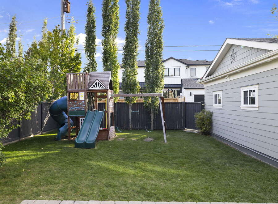 Enjoy outdoor fun in this spacious backyard featuring a vibrant playground with a twisty slide and swings, perfect for children's entertainment.