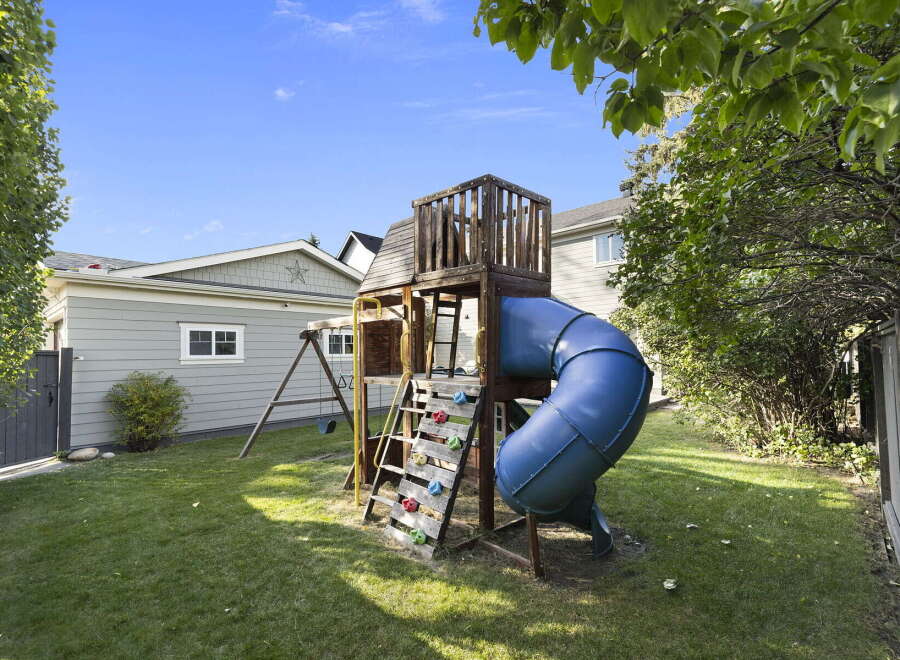 Enjoy outdoor fun in this spacious backyard featuring a vibrant blue tube slide and a classic swing set, perfect for children's entertainment.