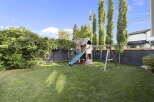 Enjoy outdoor fun in this spacious backyard featuring a vibrant green lawn and a charming wooden playset complete with a slide and swings.