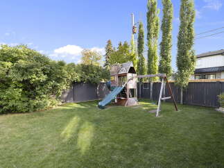 Enjoy outdoor fun in this spacious backyard featuring a vibrant green lawn and a charming wooden playset complete with a slide and swings.