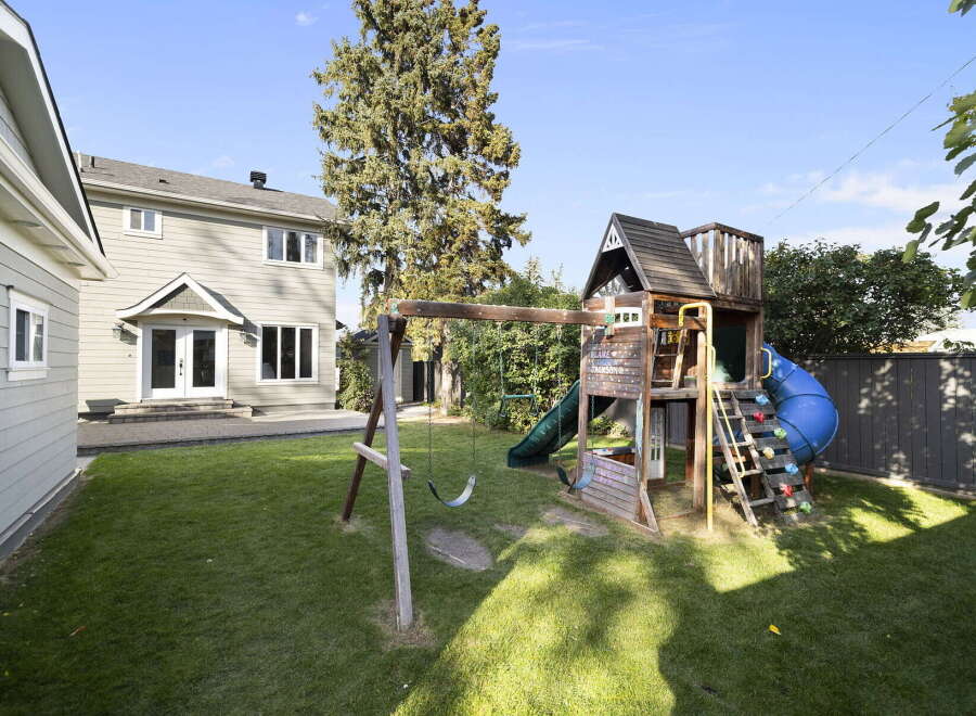 Enjoy outdoor fun in this spacious backyard featuring a large wooden playset with a slide and swings, perfect for children's entertainment.