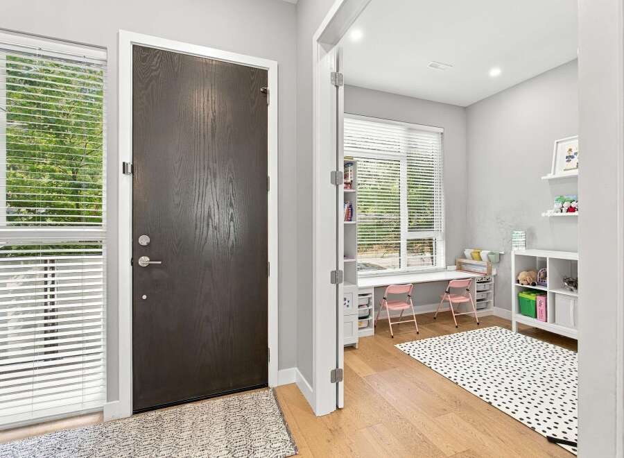 Step into a bright and airy entryway featuring a modern dark wood door and a large window with horizontal blinds.
