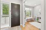 Step into a bright and airy entryway featuring a modern dark wood door and a large window with horizontal blinds.