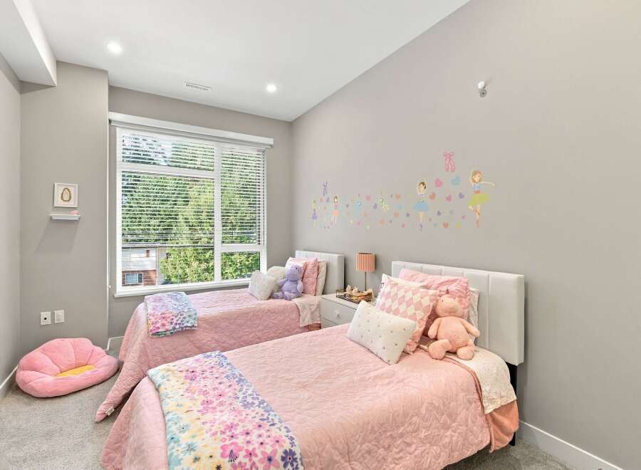 This charming children's bedroom features two twin beds adorned with pink quilted bedding and playful stuffed animals.