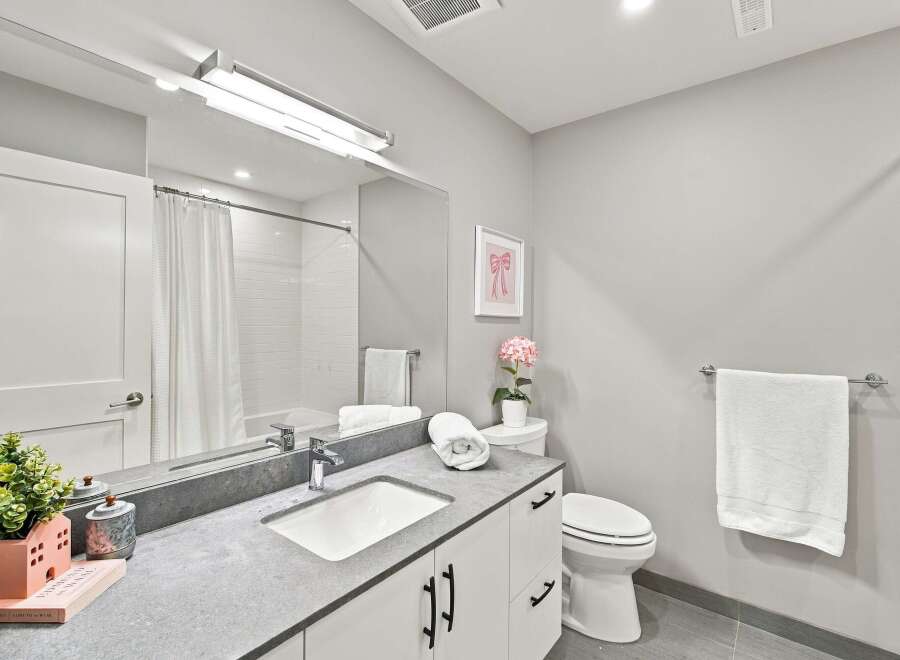 This modern bathroom features a sleek vanity with a stone countertop and a clean white sink, complemented by a large mirror and bright overhead lighting.