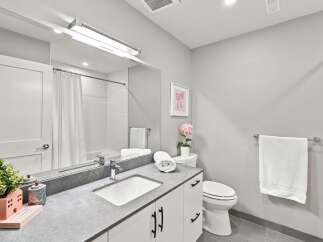This modern bathroom features a sleek vanity with a stone countertop and a clean white sink, complemented by a large mirror and bright overhead lighting.