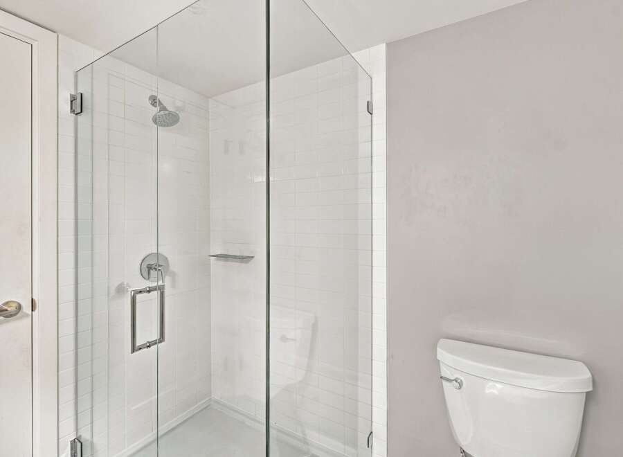 Step into this modern bathroom featuring a sleek glass-enclosed shower with a rainfall showerhead and a convenient built-in shelf.