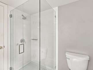 Step into this modern bathroom featuring a sleek glass-enclosed shower with a rainfall showerhead and a convenient built-in shelf.