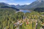 Discover this stunning aerial view of a residential neighborhood nestled amidst a lush, evergreen forest, with a serene lake and majestic mountains in the background.