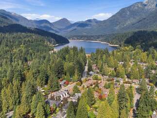 Discover this stunning aerial view of a residential neighborhood nestled amidst a lush, evergreen forest, with a serene lake and majestic mountains in the background.