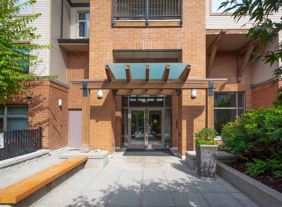 Discover modern living in this brick building featuring a welcoming entrance with a wooden pergola and glass canopy.