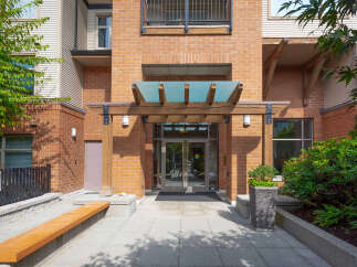 Discover modern living in this brick building featuring a welcoming entrance with a wooden pergola and glass canopy.