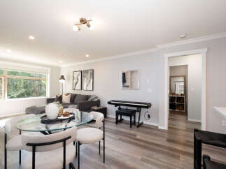 This open-concept living space features a modern sectional sofa, a glass-top dining table with upholstered chairs, and a digital piano.