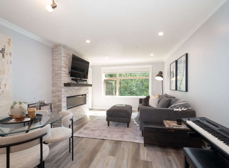 Experience modern living in this stylish open-concept space, featuring a sleek gas fireplace and a large window overlooking lush greenery.