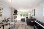 Experience modern living in this stylish open-concept space, featuring a sleek gas fireplace and a large window overlooking lush greenery.