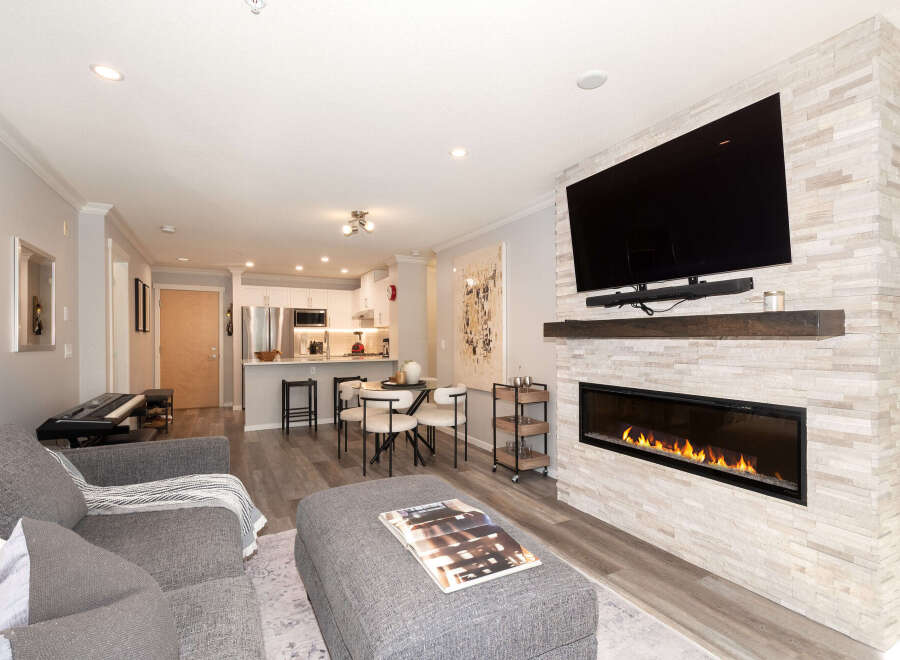 Experience modern living in this stunning open-concept condo, featuring a sleek fireplace with a stone accent wall and a large flat-screen TV.