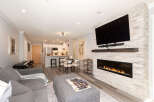 Experience modern living in this stunning open-concept condo, featuring a sleek fireplace with a stone accent wall and a large flat-screen TV.
