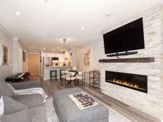 Experience modern living in this stunning open-concept condo, featuring a sleek fireplace with a stone accent wall and a large flat-screen TV.