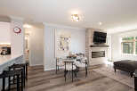 Experience modern living in this open-concept space featuring a sleek kitchen island with bar stools, a chic dining area with a glass table, and a cozy living room centered around a stone-clad fireplace with a mounted TV.