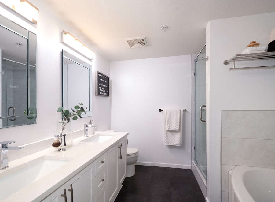 This modern bathroom features a sleek double vanity with two undermount sinks and chrome faucets, complemented by a large mirror with integrated lighting.