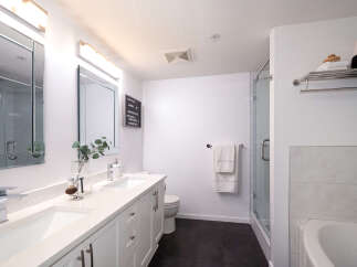This modern bathroom features a sleek double vanity with two undermount sinks and chrome faucets, complemented by a large mirror with integrated lighting.
