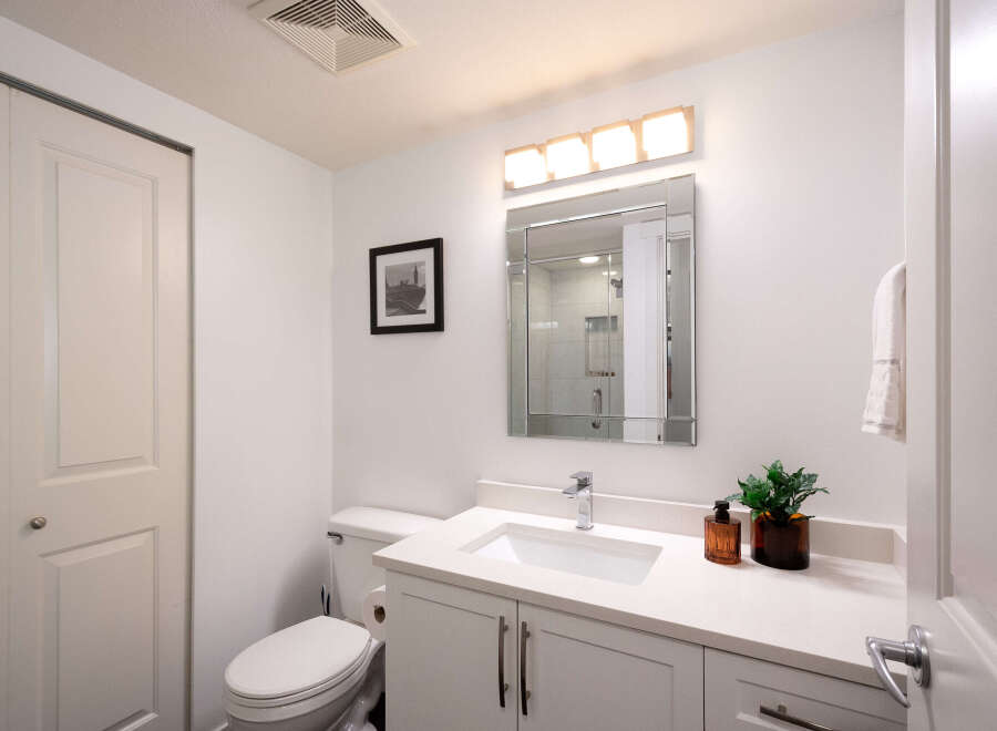 This modern bathroom features a sleek vanity with a white countertop and undermount sink, complemented by a large, beveled mirror and a stylish four-light vanity fixture.