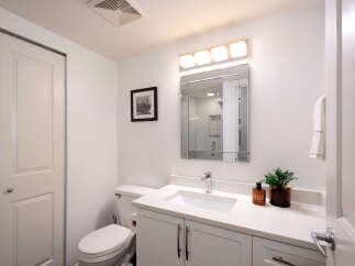 This modern bathroom features a sleek vanity with a white countertop and undermount sink, complemented by a large, beveled mirror and a stylish four-light vanity fixture.