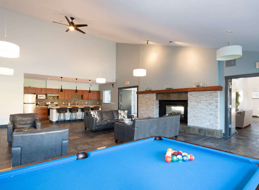 Experience ultimate relaxation and entertainment in this spacious common area, featuring a modern kitchen, a cozy fireplace, and a vibrant pool table.