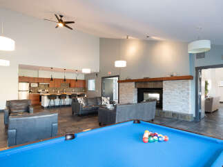Experience ultimate relaxation and entertainment in this spacious common area, featuring a modern kitchen, a cozy fireplace, and a vibrant pool table.