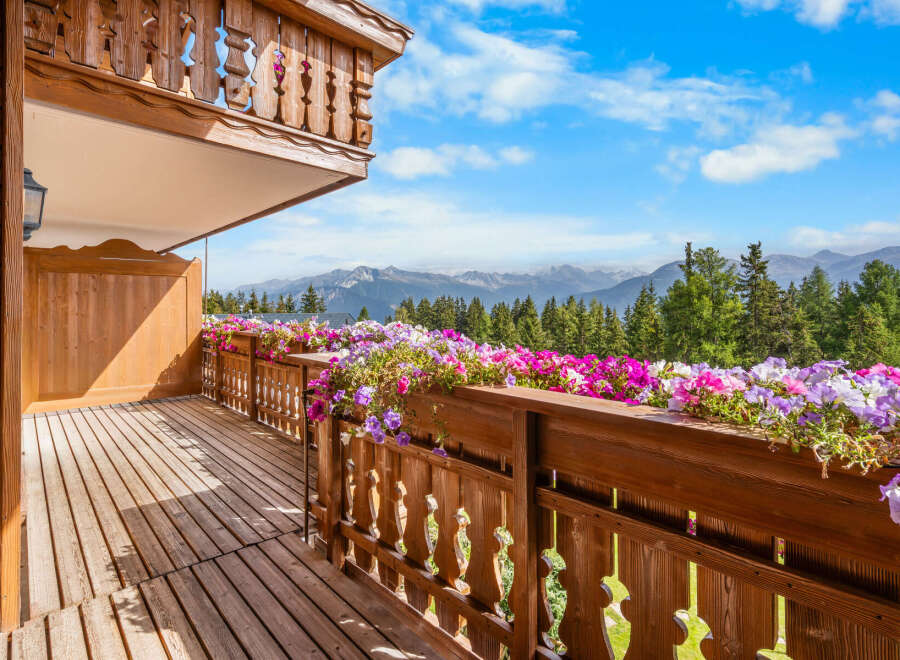 Experience breathtaking mountain views from this charming wooden balcony, adorned with vibrant flower boxes.