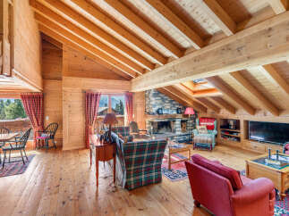 Experience rustic charm in this beautifully appointed living room, featuring a grand stone fireplace and exposed wooden beams that create a warm, inviting atmosphere.