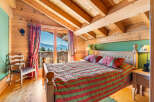 Experience cozy mountain living in this charming chalet bedroom, featuring a comfortable bed adorned with festive linens and a stunning view of snow-capped peaks from the balcony.