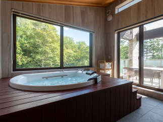 Indulge in ultimate relaxation in this luxurious bathroom featuring a spacious jacuzzi tub surrounded by warm wood accents and large windows offering serene forest views.