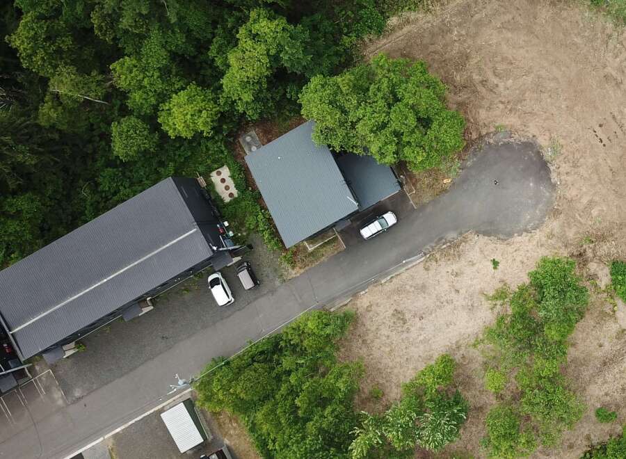 Discover this expansive property featuring a modern, dark-roofed building nestled amidst lush greenery.