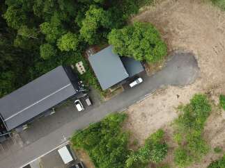 Discover this expansive property featuring a modern, dark-roofed building nestled amidst lush greenery.