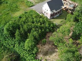 Discover this stunning property featuring a modern, multi-story house with a dark roof and light-colored siding, nestled amidst lush greenery.