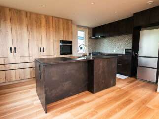 Experience modern living in this stunning kitchen featuring sleek, wood-grain cabinetry and a dramatic dark stone island.