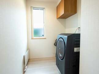 Discover this modern laundry room featuring a sleek black front-load washing machine and a convenient wall-mounted wooden cabinet for storage.