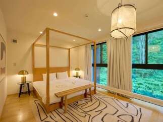 Experience serene living in this beautifully appointed bedroom featuring a luxurious four-poster bed and large windows offering stunning forest views.