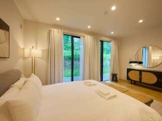 Experience serene living in this beautifully appointed bedroom, featuring a plush king-sized bed and direct access to lush outdoor views through expansive glass doors.