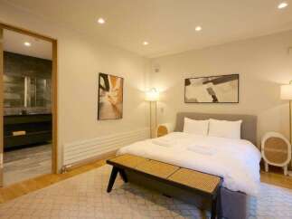 Experience modern comfort in this beautifully appointed bedroom, featuring a plush king-sized bed with crisp white linens and a stylish woven bench at its foot.
