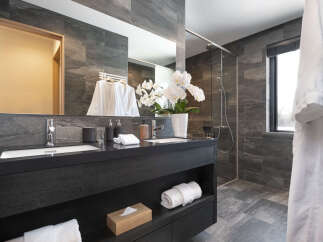 Experience modern luxury in this stunning bathroom featuring a sleek dark wood vanity with dual sinks and elegant stone tilework.