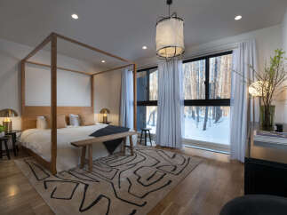 Experience serene winter living in this beautifully appointed bedroom, featuring a striking wooden four-poster bed and large windows offering breathtaking views of a snow-covered forest.