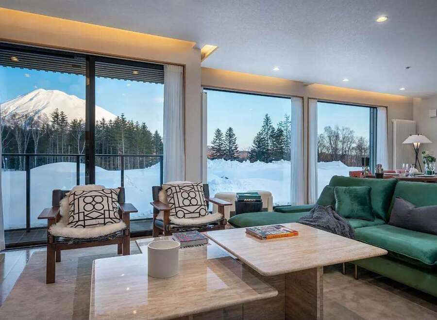 Experience breathtaking mountain views from this luxurious living room, featuring floor-to-ceiling windows that showcase a snow-covered landscape and majestic peak.