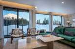Experience breathtaking mountain views from this luxurious living room, featuring floor-to-ceiling windows that showcase a snow-covered landscape and majestic peak.