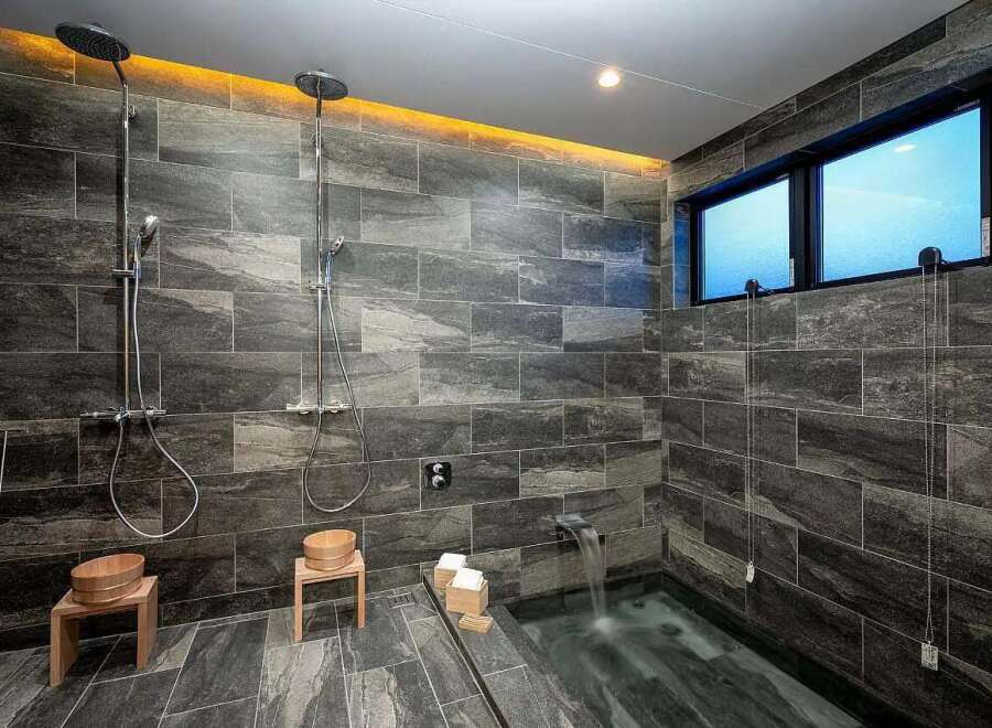 Experience ultimate relaxation in this modern bathroom featuring dual rain showerheads and a deep soaking tub with a waterfall faucet.