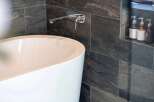 Experience modern luxury in this bathroom, featuring a sleek freestanding bathtub and a minimalist wall-mounted faucet.