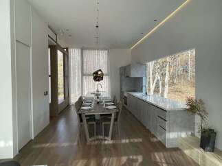 Experience modern living in this stunning open-concept space, featuring a sleek dining area and a contemporary kitchen with a large picture window overlooking a serene forest.