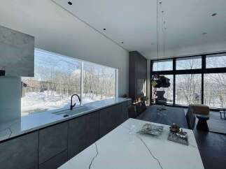 Experience modern living in this stunning home featuring a sleek, minimalist kitchen with a large island and expansive windows offering breathtaking winter views.
